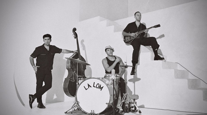 A black and white image of three men dressed in black by a staircase with instruments